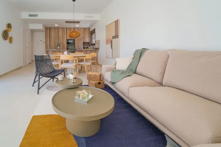 Séjour de la villa témoin avec canapé, table basse et tapis, et le coin repas et la cuisine au fond